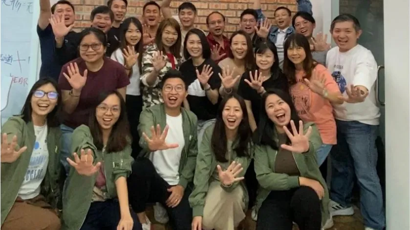 A large team waving in front of a workshop wall of notes